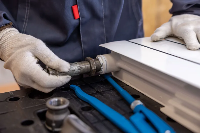 Plumber's gloved hands fitting a pipe to a radiator