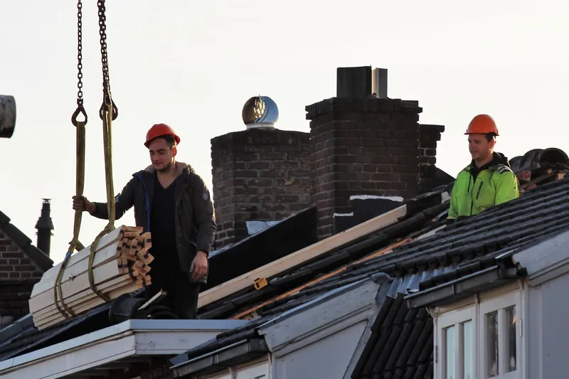 Roofing crew in hard hats guiding a crane load of lumber onto a house roof